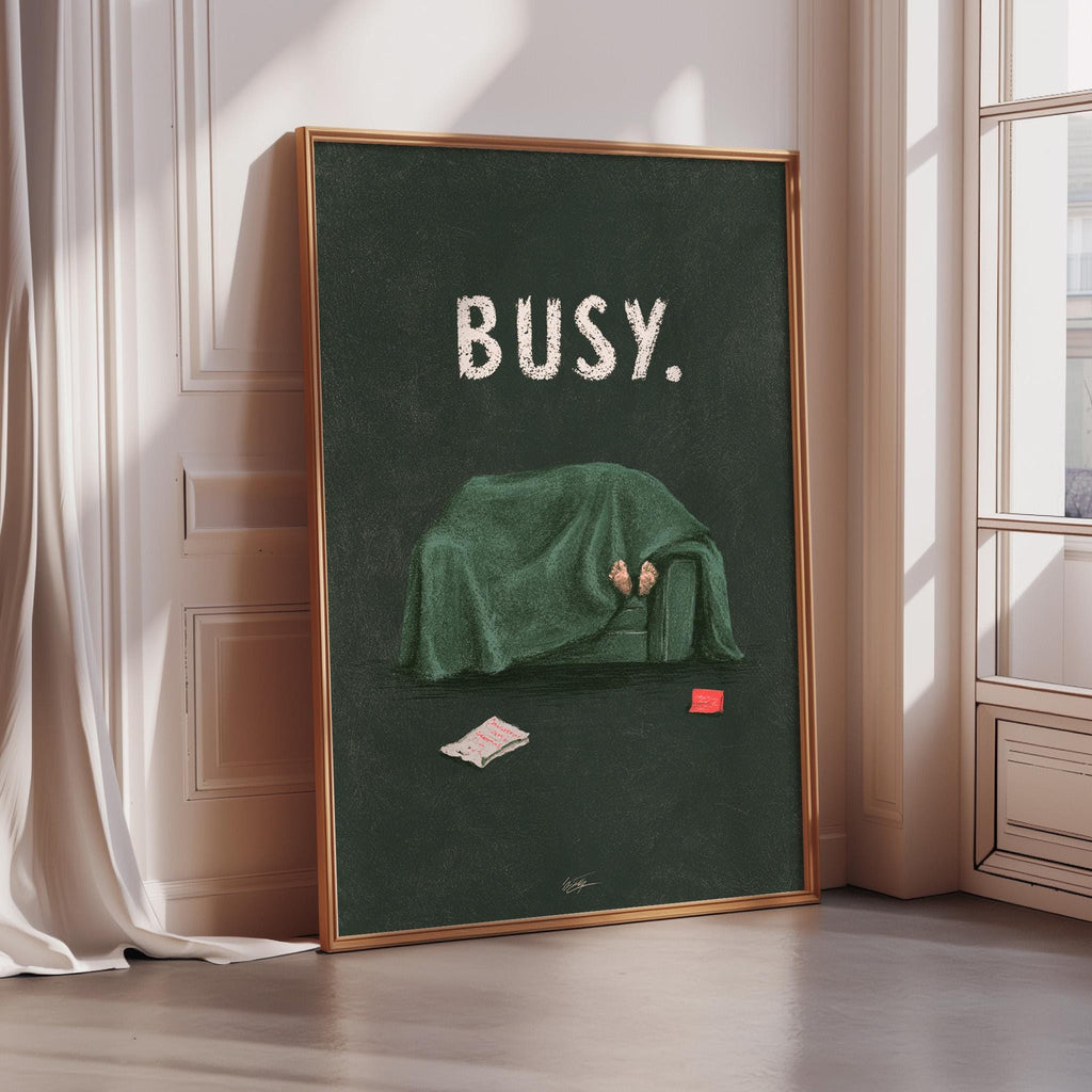 A framed poster with the word "BUSY" written on it, depicting a person lying on a couch covered with a green blanket.