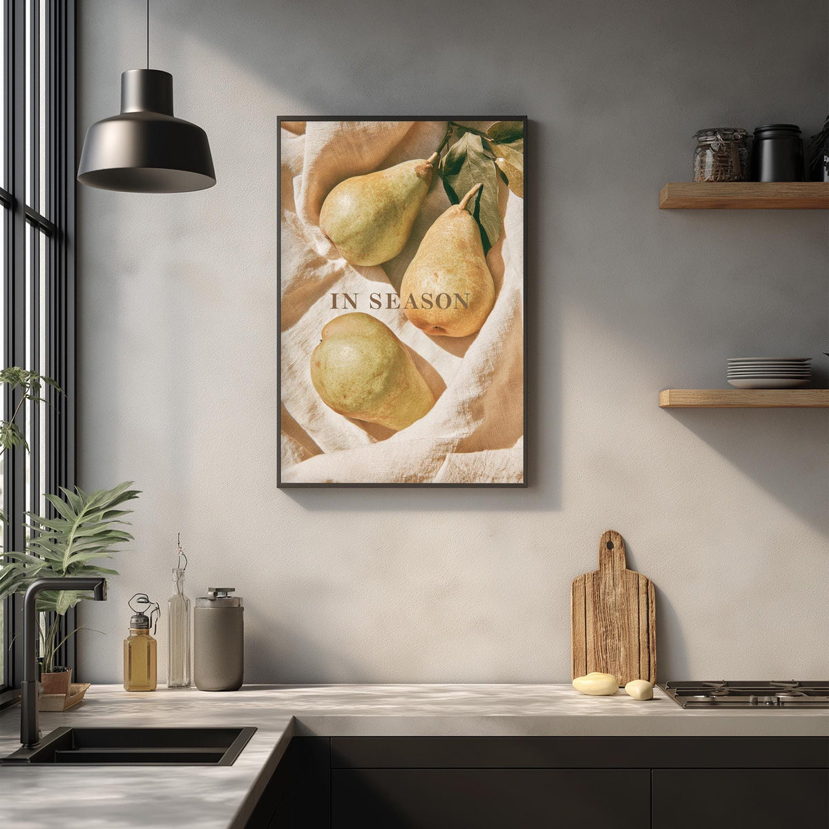 a kitchen counter with a framed picture of pears hanging on the wall above it. The pears are arranged in a visually appealing manner, and the phrase "IN SEASON" is displayed on the picture.