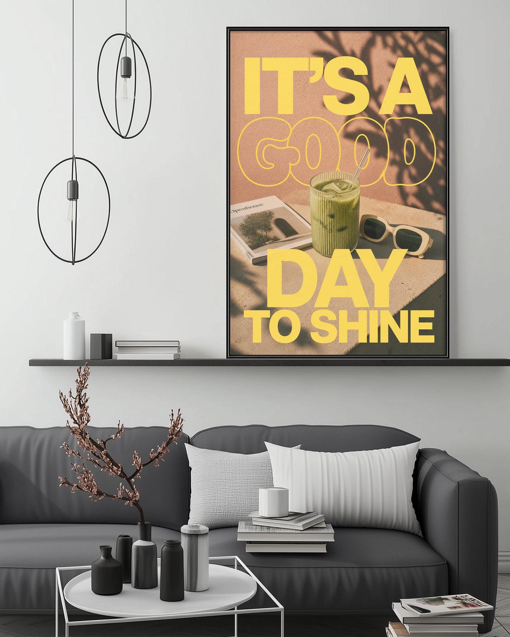 a modern living room with a gray sofa, a coffee table, and a large framed poster with the text "IT'S A GOOD DAY TO SHINE" displayed on the wall above the sofa.