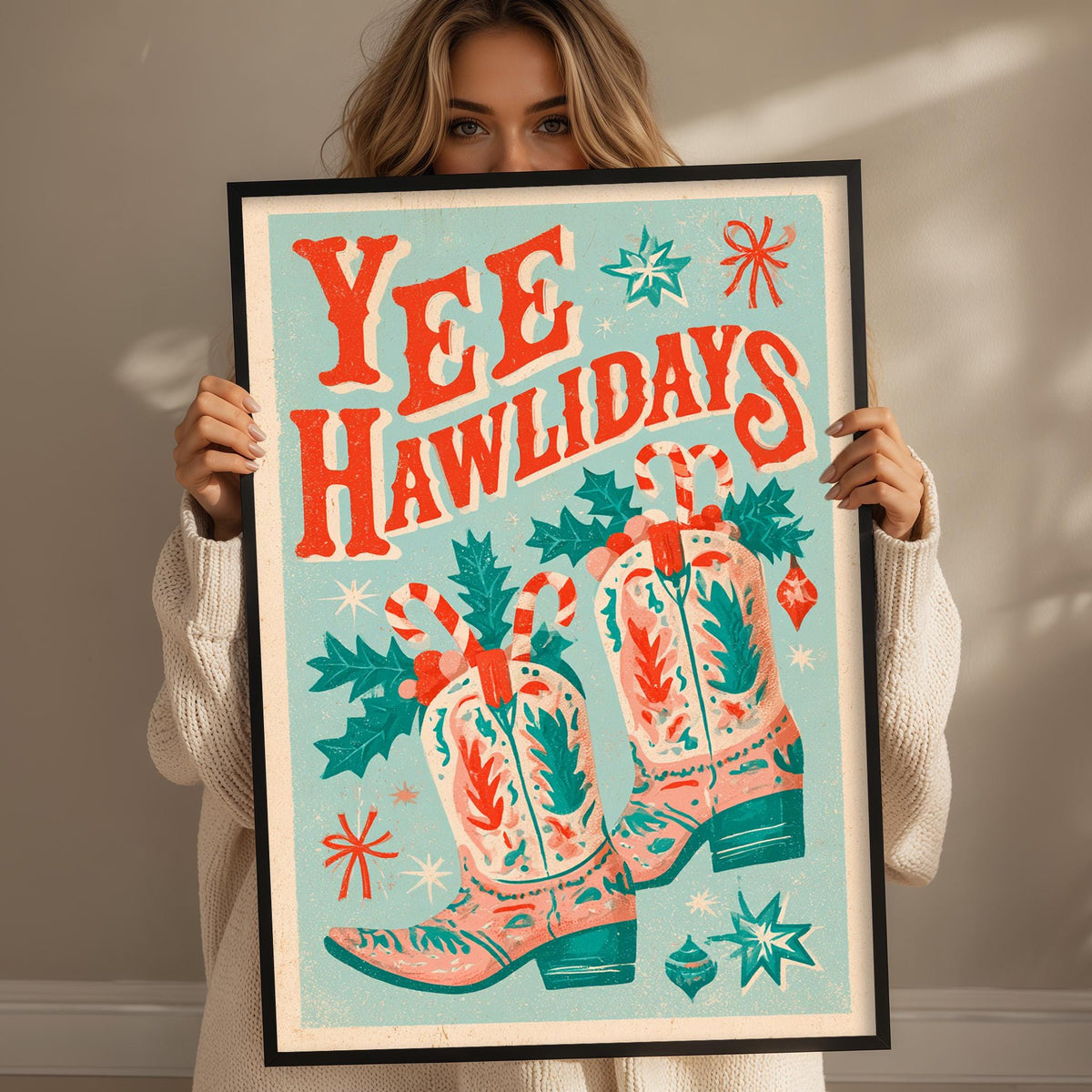 A woman is holding up a framed poster with a festive design featuring cowboy boots, Christmas decorations, and the text "YEEhawlidays".