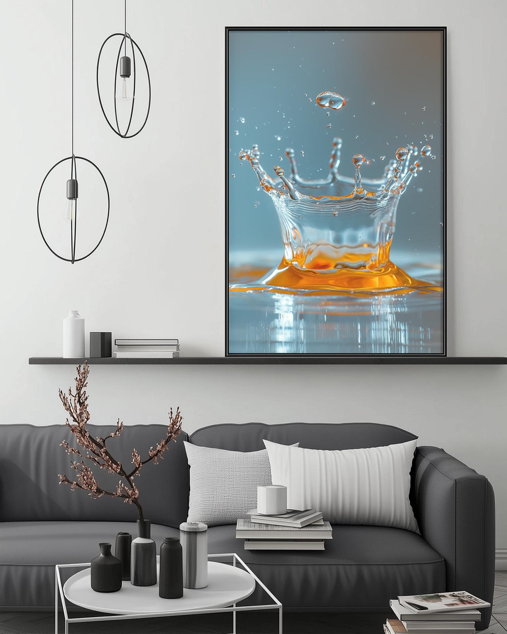 a large framed photograph of a splash of water on a wall, with a black and white color scheme. The photograph is displayed above a gray couch with a coffee table in front of it. The room has a minimalist and modern design, with a black pendant light hanging from the ceiling and a white shelf below the couch.
