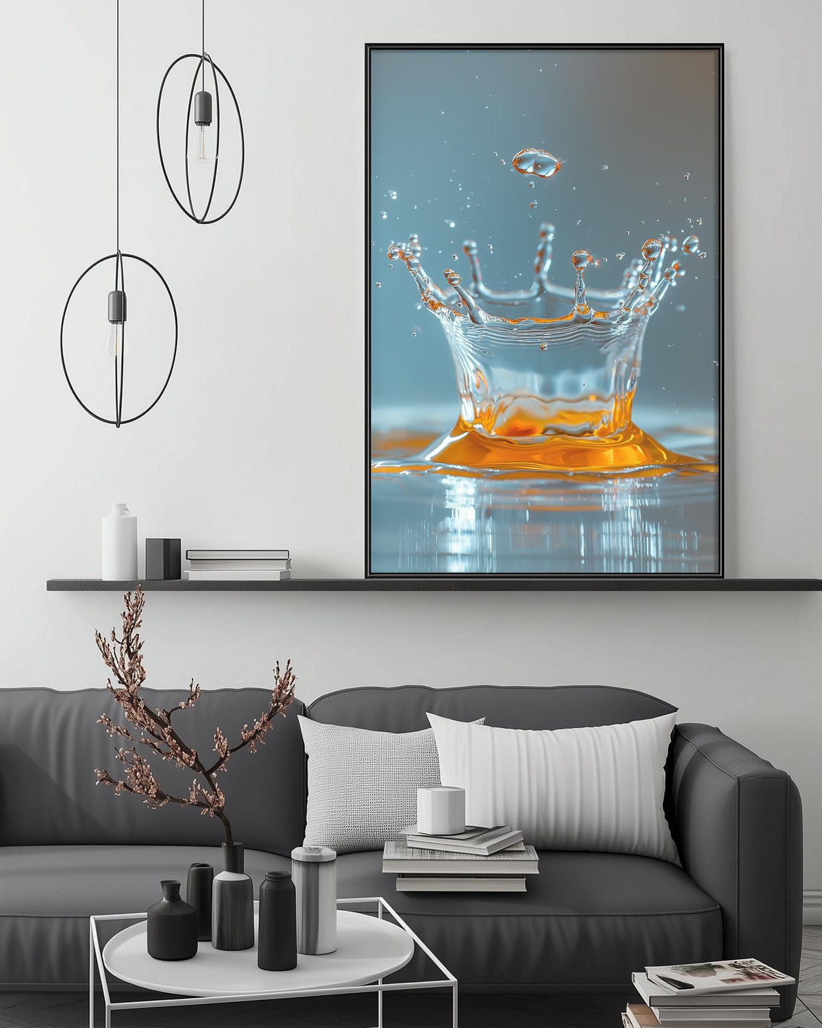 a large framed photograph of a splash of water on a wall, with a black and white color scheme. The photograph is displayed above a gray couch with a coffee table in front of it. The room has a minimalist and modern design, with a black pendant light hanging from the ceiling and a white shelf below the couch.