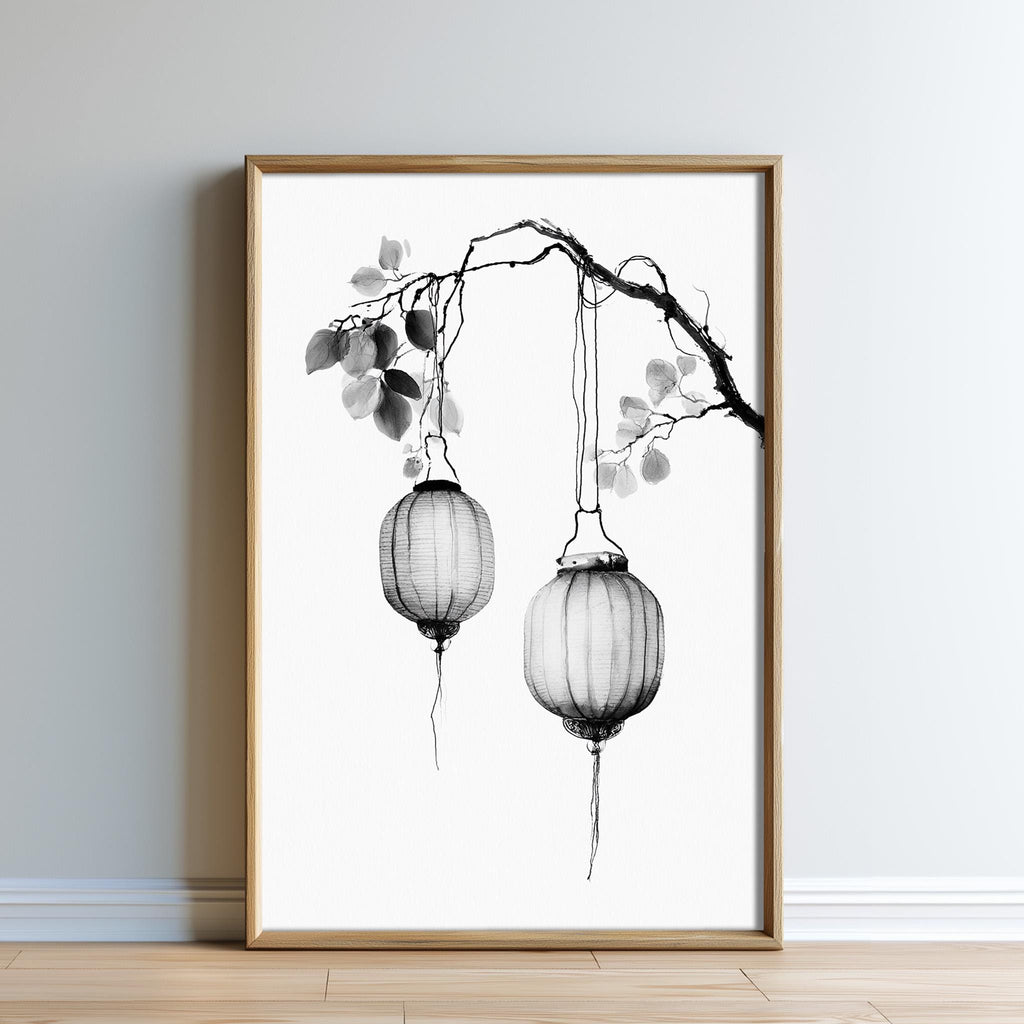 A framed black and white image depicting two hanging lanterns on a branch.