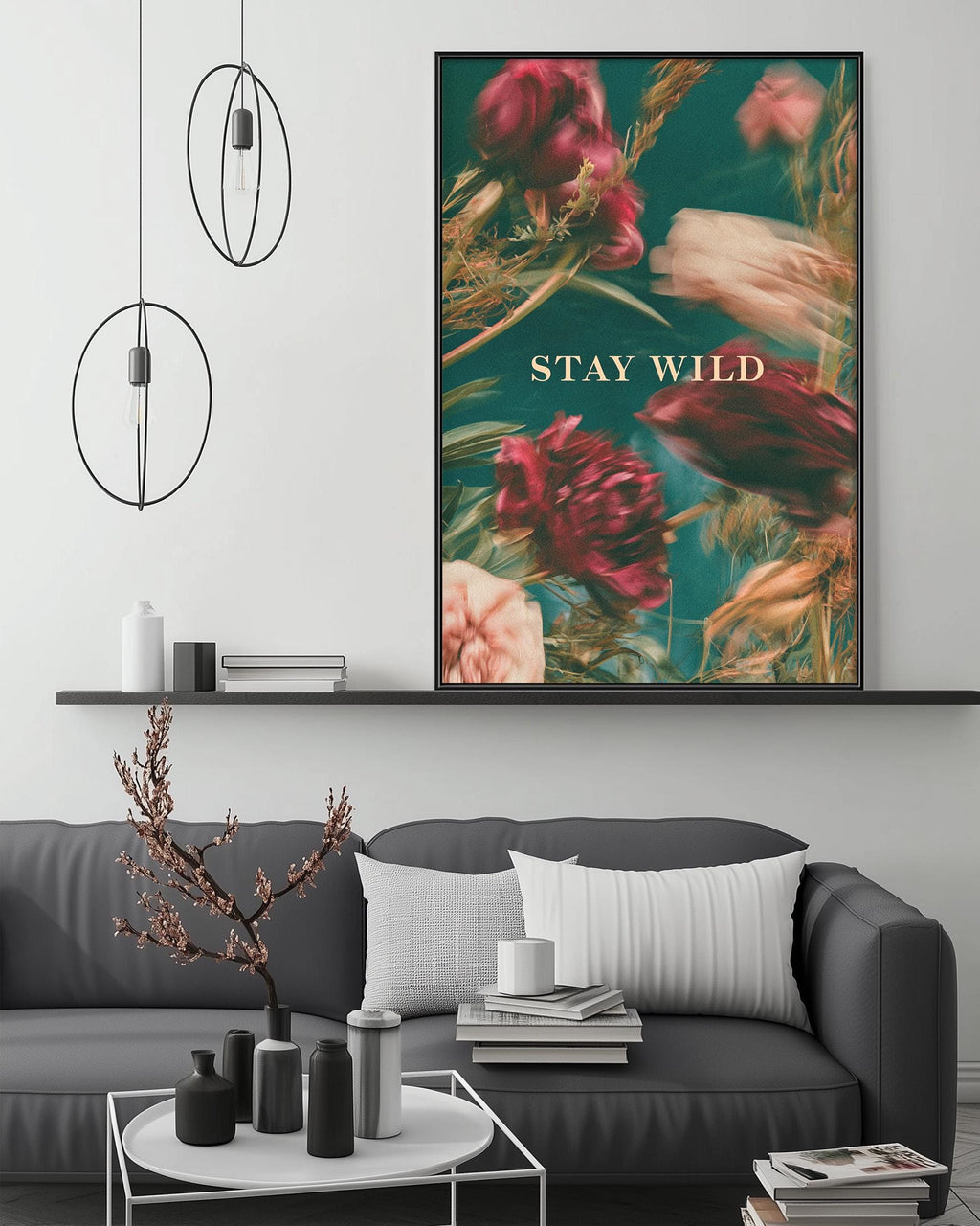 a modern living room with a gray sofa, a coffee table, and a large framed poster of flowers on the wall. The poster has a green background and displays the text "STAY WILD" in white letters.