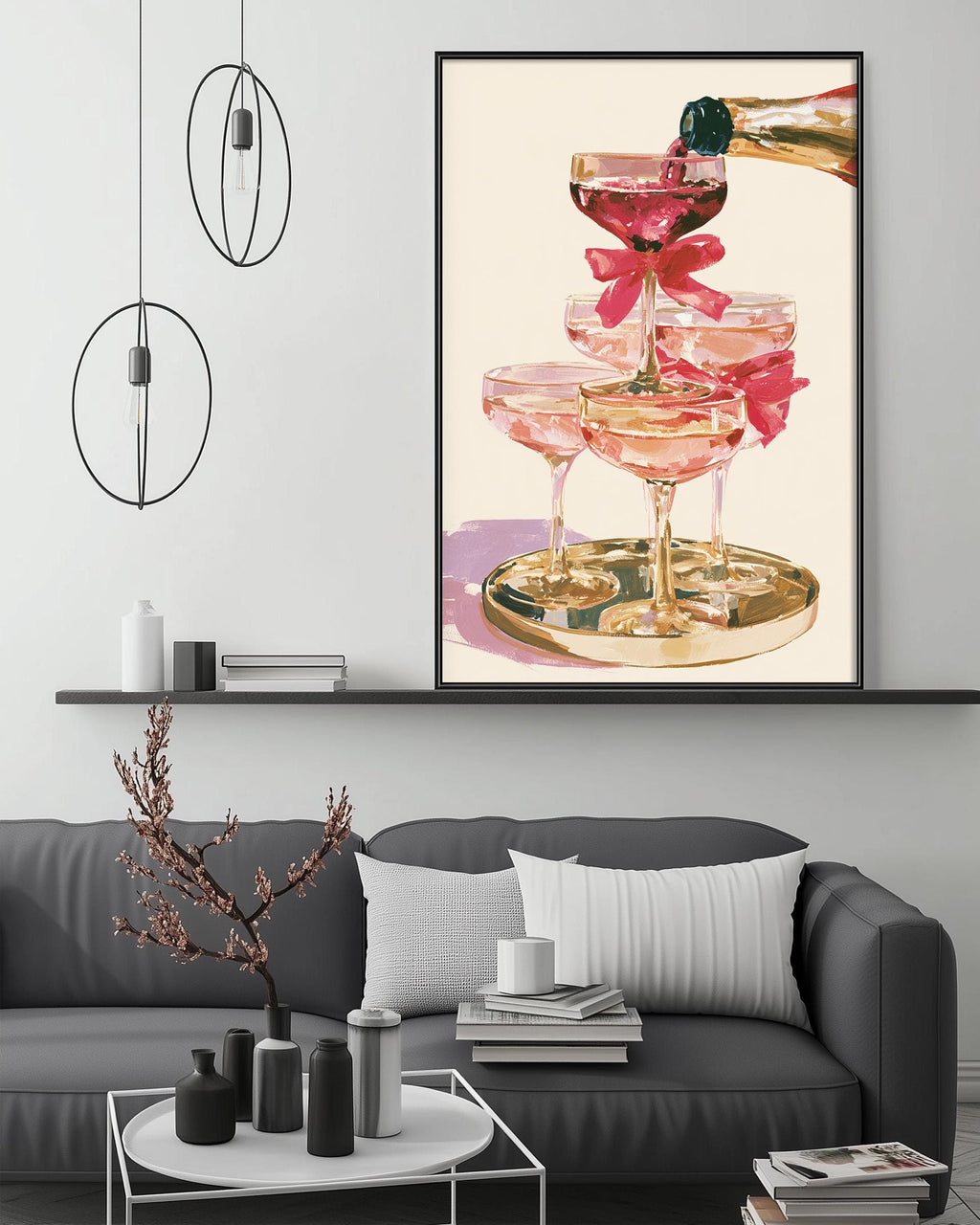 a large framed artwork depicting a glass of pink champagne with a bow, hanging on a wall above a gray couch with a coffee table in front of it.