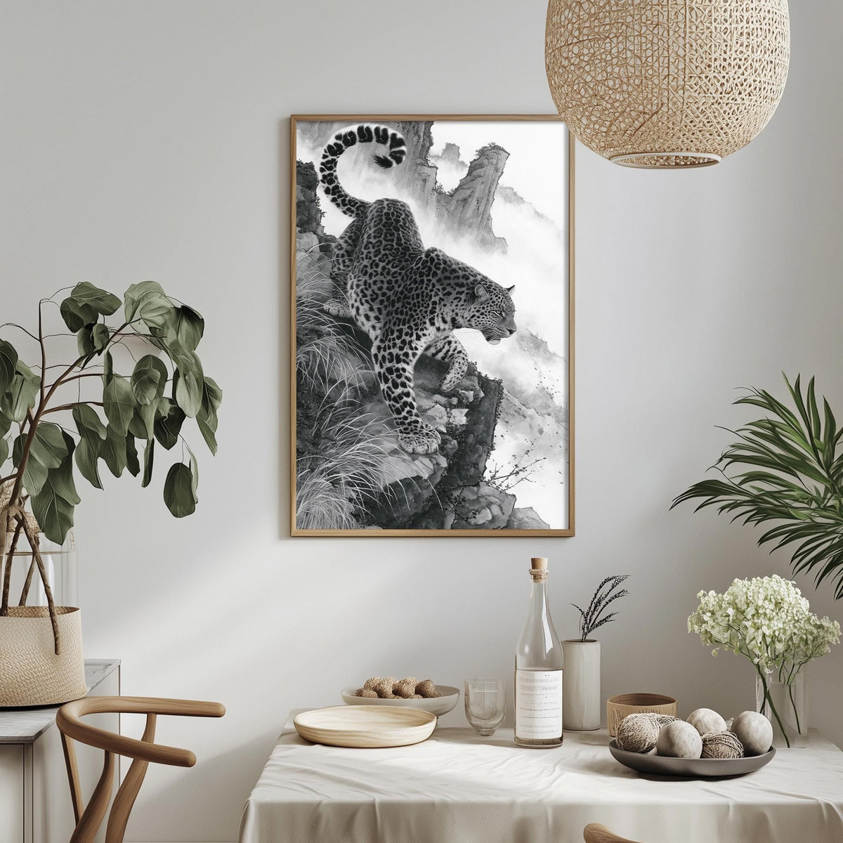 a framed black and white photograph of a leopard on a rocky cliff, hanging on a wall above a dining table with various decorative items and plants.