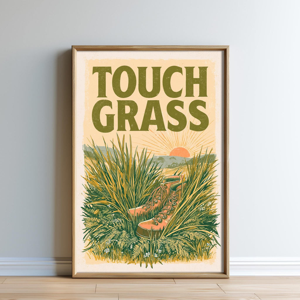 The image is a framed poster with a vibrant illustration of tall grass and a pair of hiking boots, with the text "TOUCH GRASS" prominently displayed.