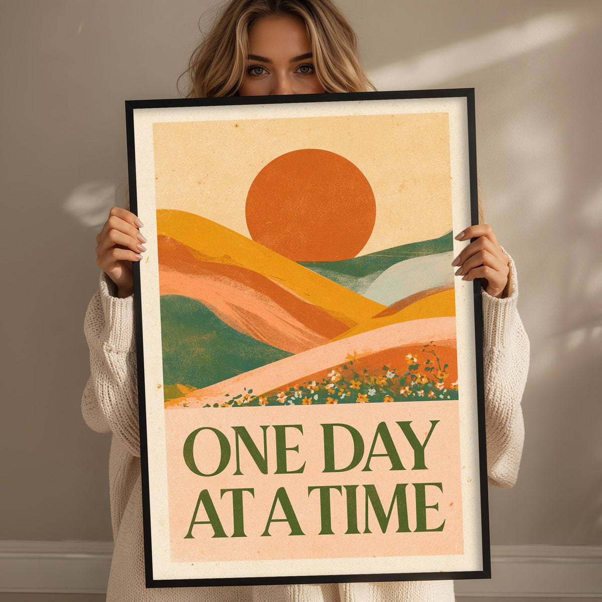 A woman holding a framed poster with a landscape and a large sun in the background.