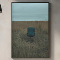 a minimalist kitchen interior with a framed picture of a chair in a field hanging on the wall above a countertop with various kitchen items.