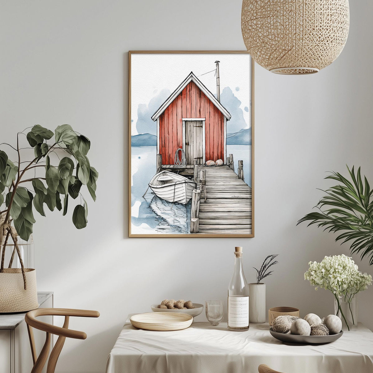 a framed painting of a red wooden cabin with a dock and boat, hanging on a wall above a dining table with various decorative items and plants.