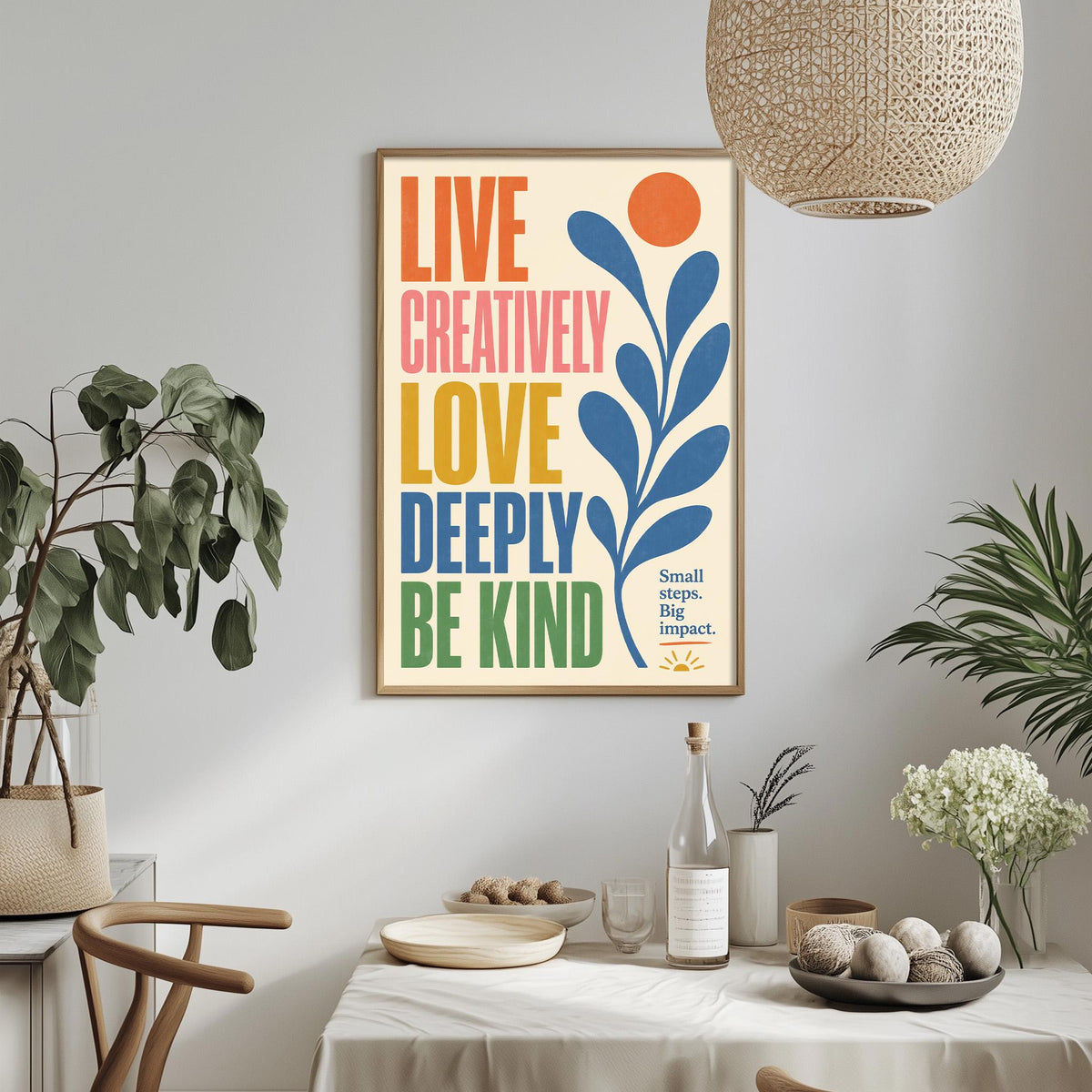 a framed poster with the text "LIVE CREATIVELY LOVE DEPTHY BE KIND" displayed on a wall above a dining table with various items on it.