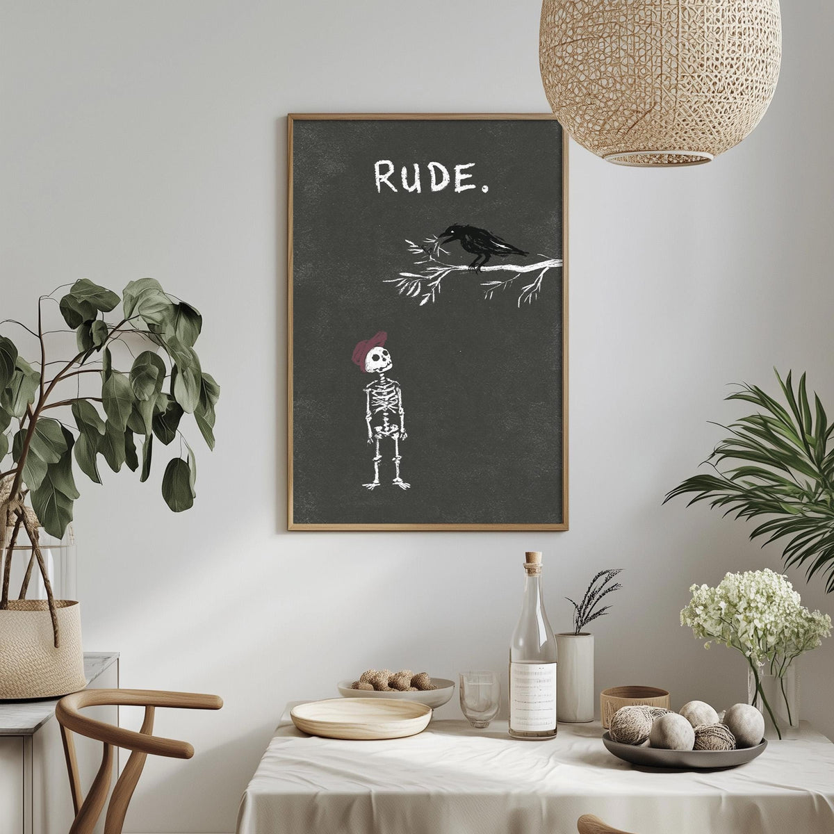 a dining table with a bowl of fruit, a bottle, and a vase of flowers, along with a potted plant and a hanging light fixture. Above the table, there is a framed poster with a skeleton and a bird, and the word "Rude" written on it.