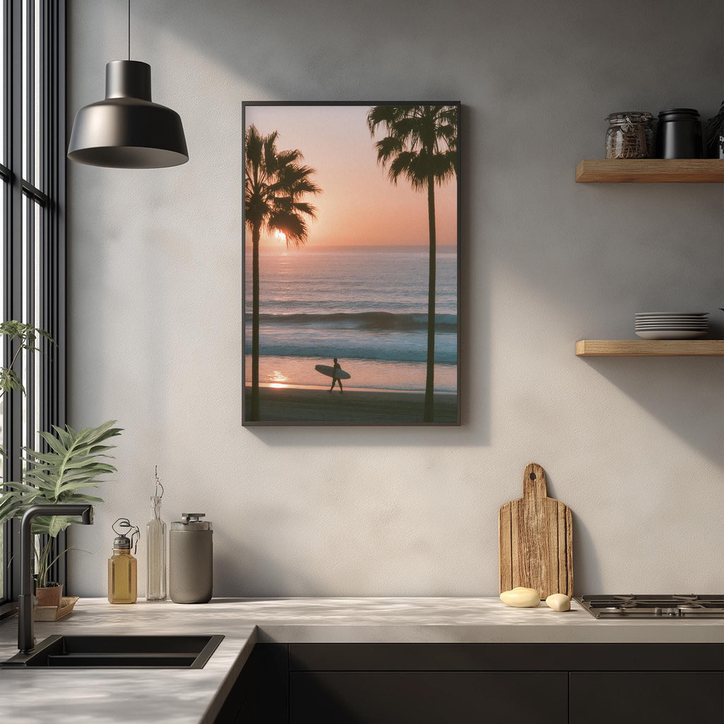 a kitchen counter with a framed picture of a surfer on the wall, depicting a sunset over the ocean.