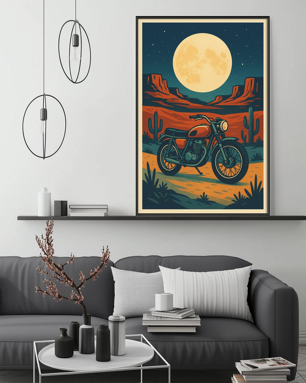 a large framed poster of a motorcycle on a desert landscape, with a full moon in the background. The poster is hanging on a wall above a gray couch, which has a coffee table in front of it. The room also has some decorative elements, such as pendant lights, a vase, and a stack of books.
