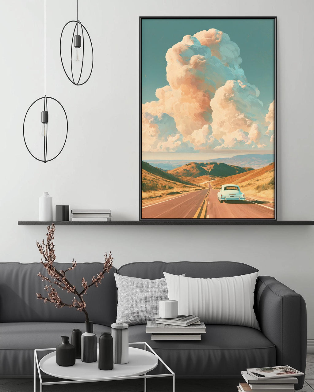 a large framed painting of a road with a car driving down it, set against a backdrop of a cloudy sky. The painting is hung on a wall above a gray couch, which has a coffee table in front of it. The room also includes a shelf with decorative items and a potted plant.