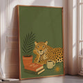 A framed poster depicting a leopard resting on a bookshelf with a cup of coffee and a plant, set against a green background.