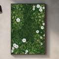 a kitchen counter with a framed picture of white flowers on a green background hanging above it. The counter has various kitchen items, such as a cutting board, a soap dispenser, and a bottle.