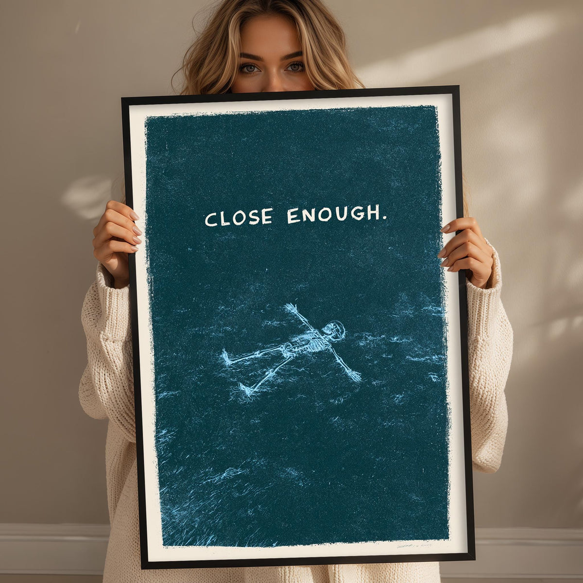 A woman is holding up a framed poster with the text "CLOSE ENOUGH" on it.