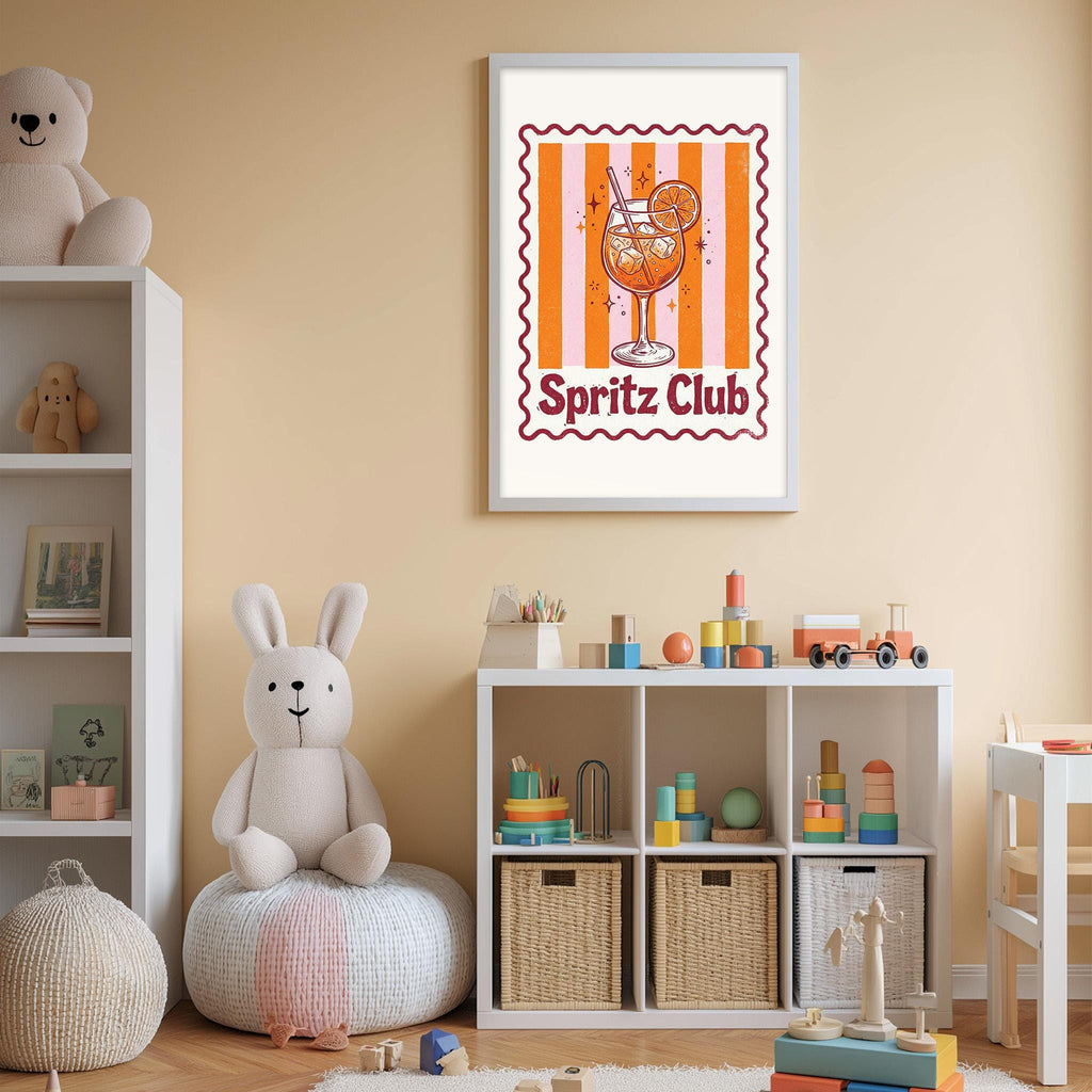 A child's bedroom with a white bookshelf, a stuffed rabbit, and a toy train. Above the bookshelf is a framed poster featuring an illustration of a glass of champagne with a tiger logo.