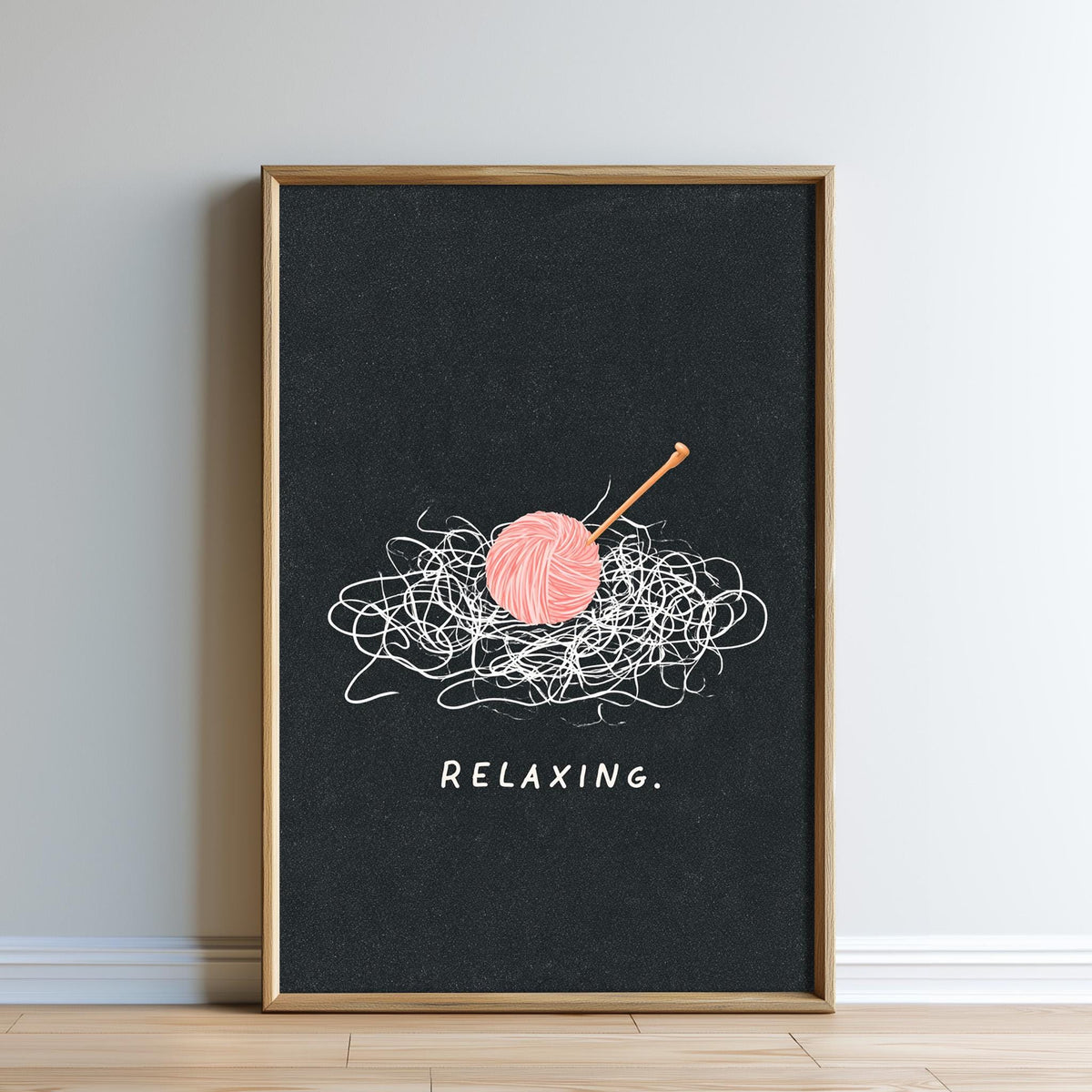 A framed poster with a black background and a pink ball of yarn. The yarn is tangled and appears to be relaxing. The word "RELAXING" is written below the image.