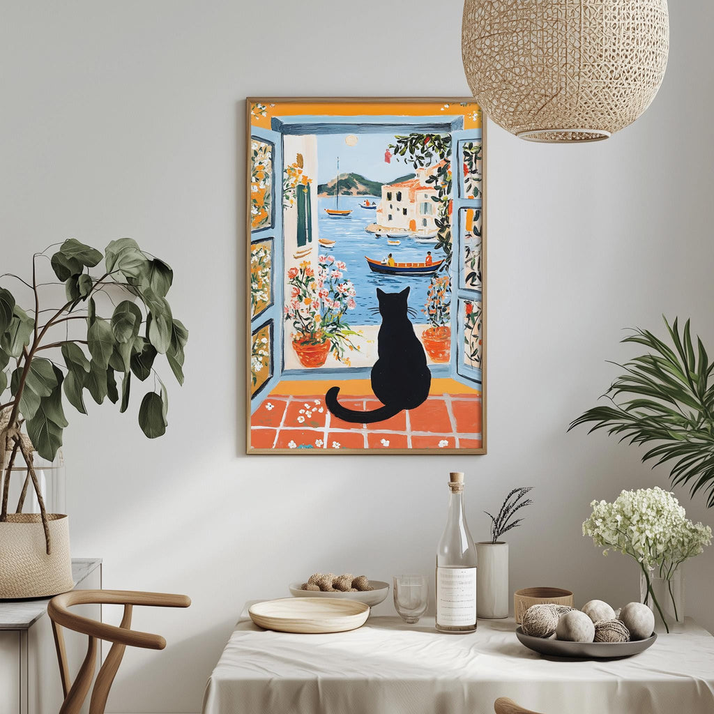 a dining table with a white tablecloth, a bowl of fruit, a bottle, and a vase with flowers. Above the table, there is a framed painting depicting a black cat sitting on a windowsill, looking out at a boat on the water.
