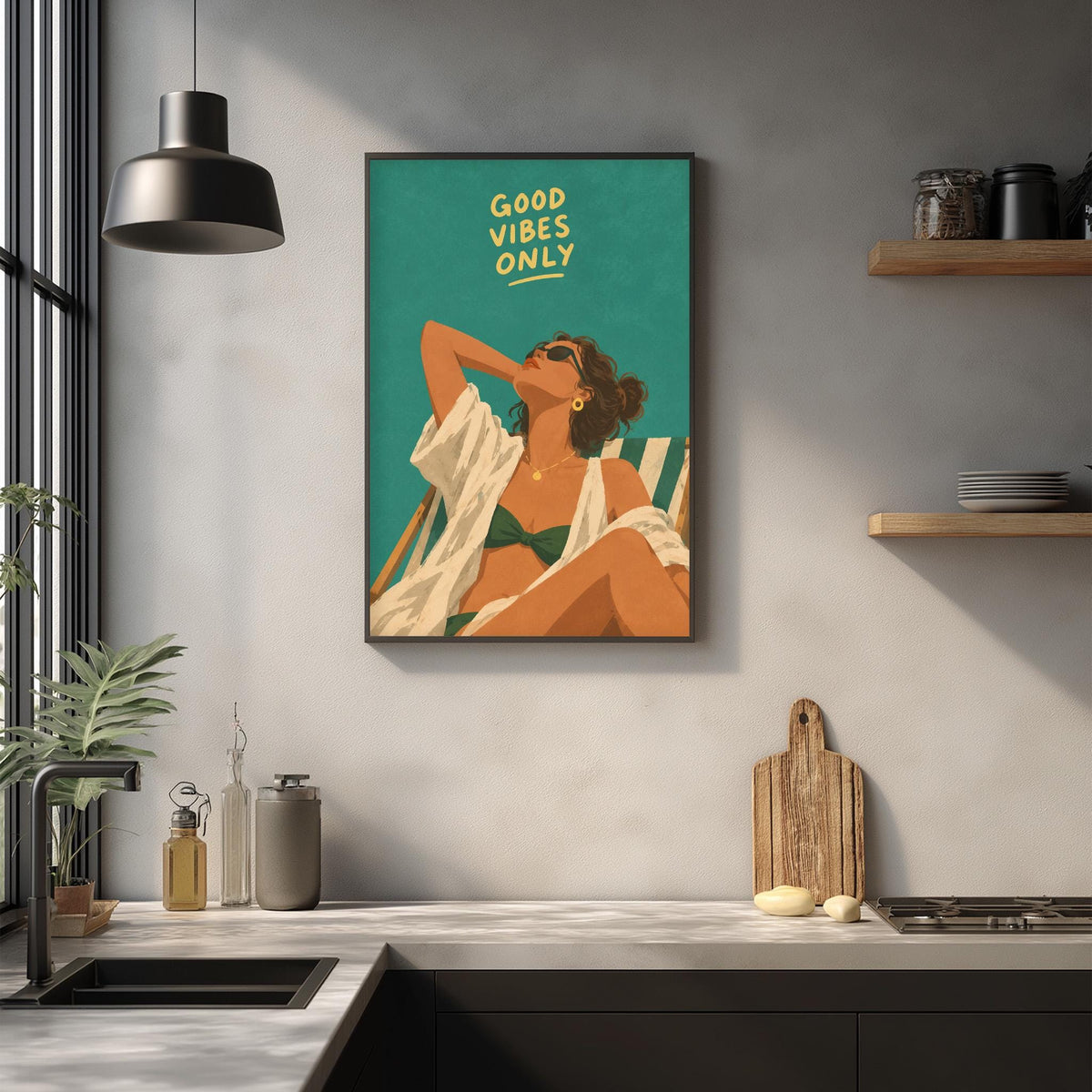 a framed poster of a woman relaxing in a lounge chair, with the text "Good Vibes Only" written above her. The poster is hanging on a wall above a kitchen counter with various kitchen items such as a cutting board, a bottle, and a bowl.