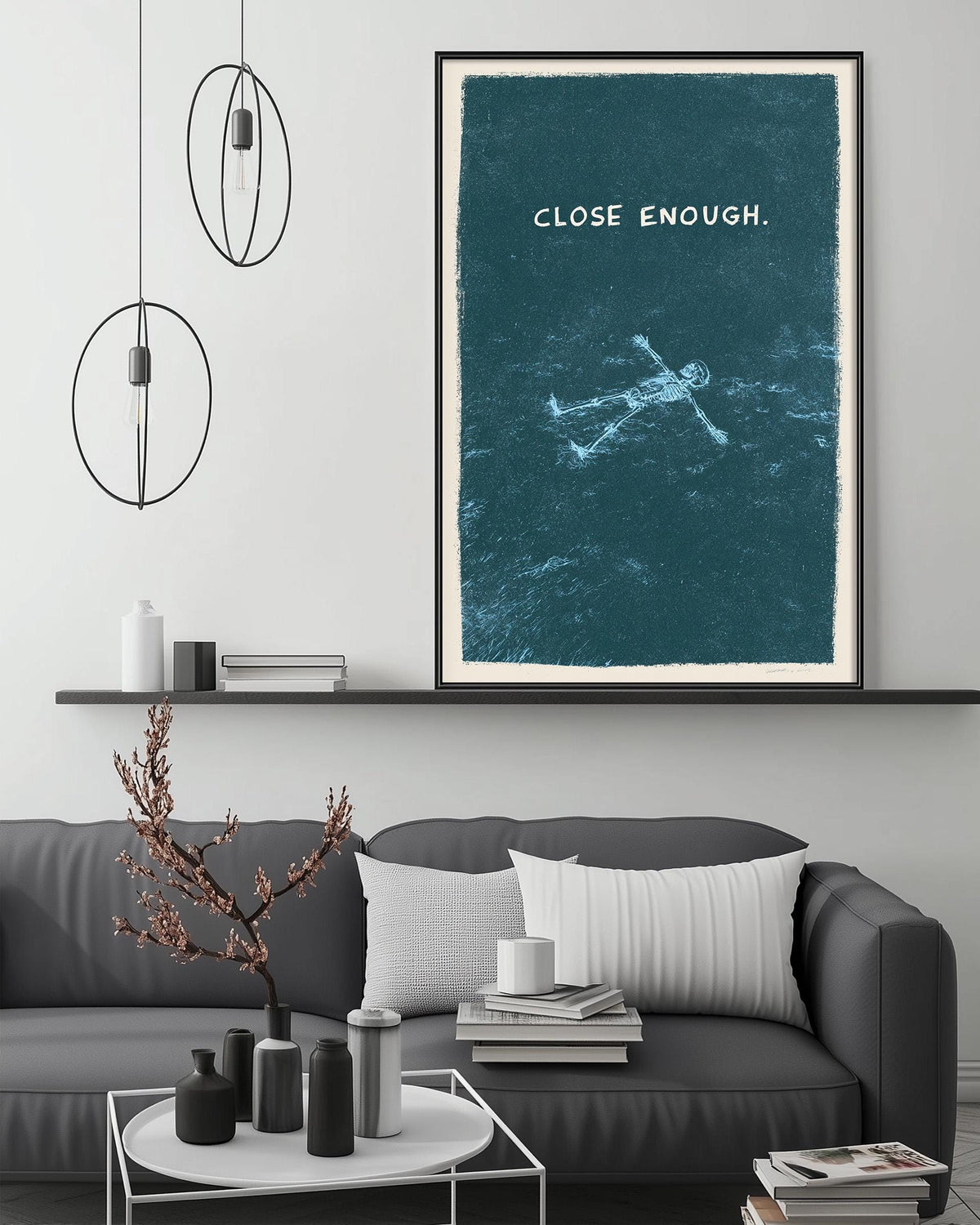 a modern living room with a gray sofa, a coffee table, and a framed poster on the wall. The poster depicts a person floating in a blue ocean, accompanied by the text "CLOSE ENOUGH."