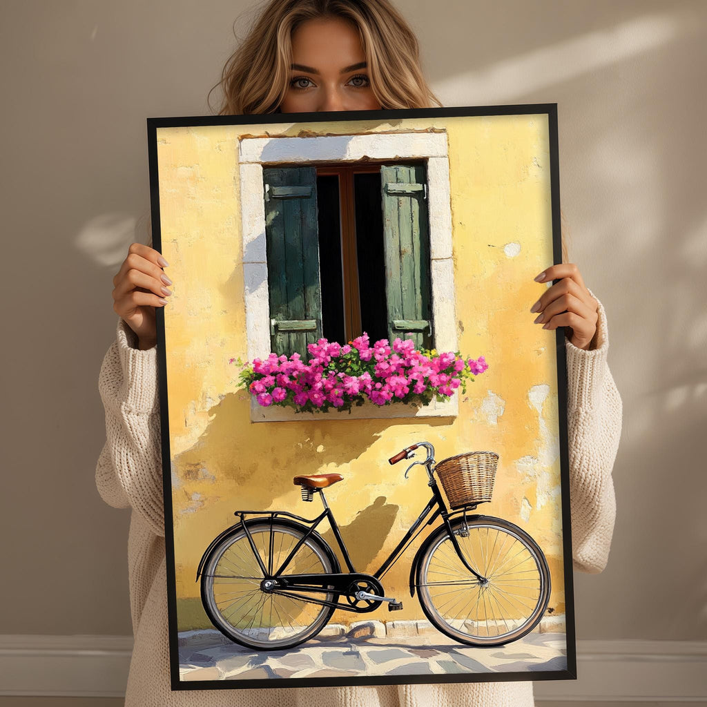 A woman holds up a framed image depicting a bicycle with a basket and a window with pink flowers.