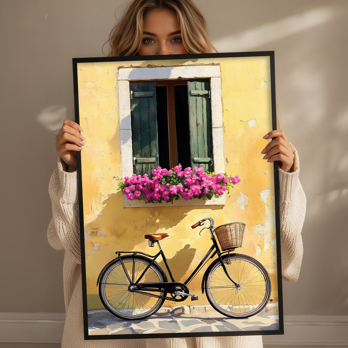 A woman holds up a framed image depicting a bicycle with a basket and a window with pink flowers.