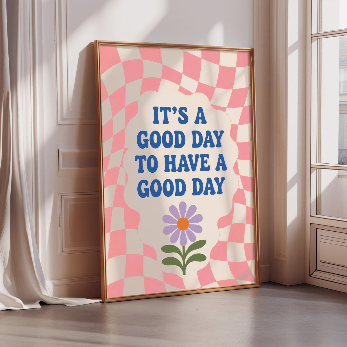 A framed poster with a checkered pink and white background, featuring a flower and the text "IT'S A GOOD DAY TO HAVE A GOOD DAY"