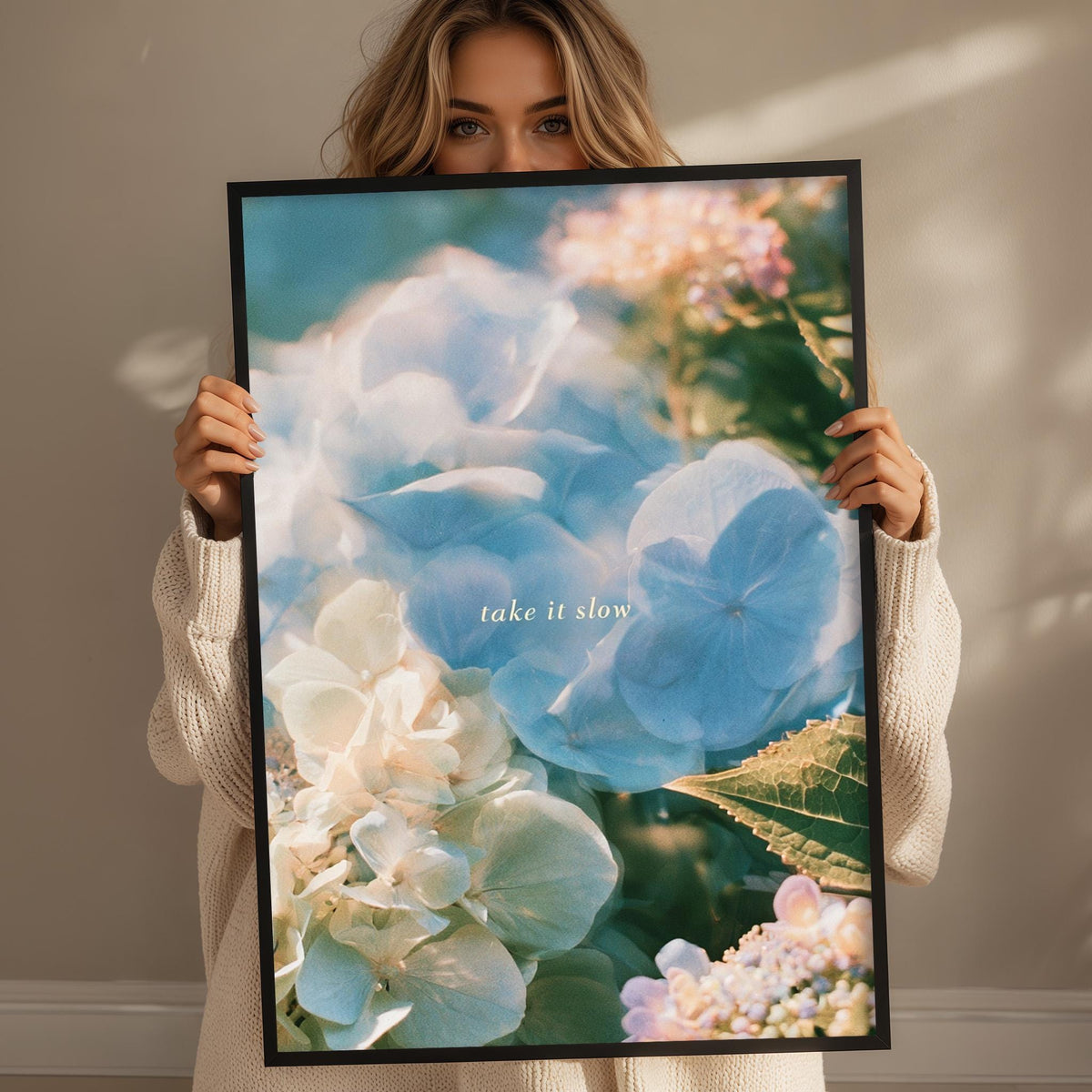 A woman holding a framed picture of flowers, with the text "Take it slow" written on the picture.