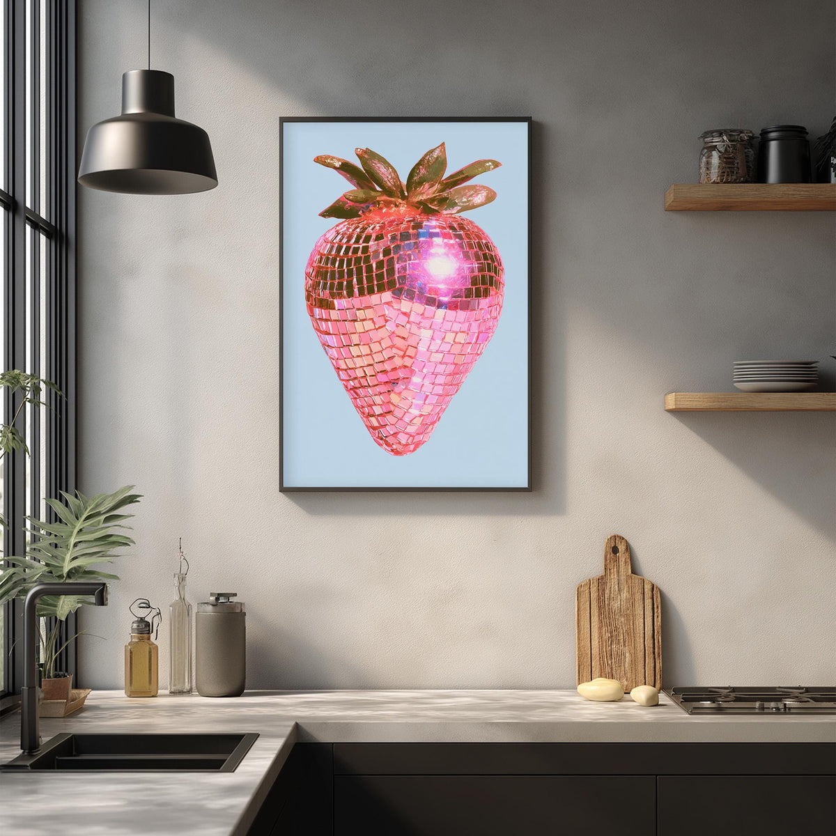 a framed artwork of a pink disco ball-patterned strawberry hanging on a wall above a kitchen counter.