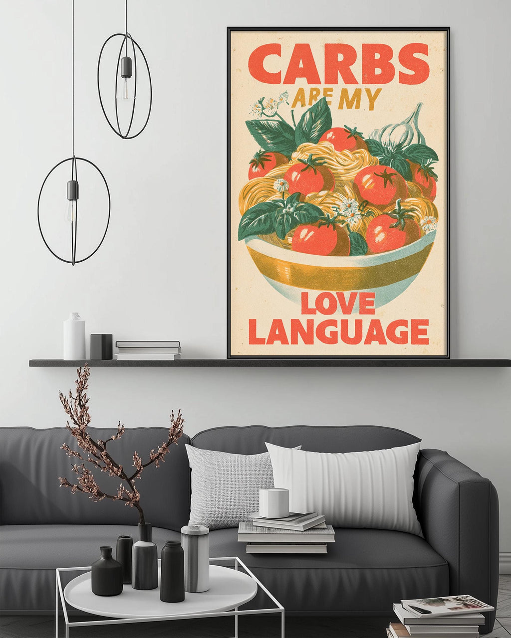 a framed poster with a vibrant illustration of a bowl of fresh vegetables, including tomatoes, garlic, and herbs, accompanied by the text "CARBS ARE MY LOVE LANGUAGE". The poster is displayed on a wall above a gray couch, which is situated in a cozy living room setting.