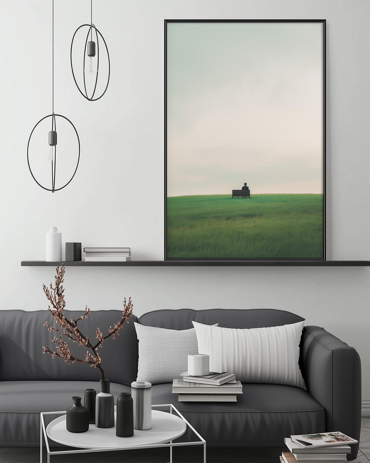 a modern living room with a gray sofa, a coffee table, and a large framed picture of a field with a building in the distance. The room has a minimalist and contemporary design, with a black and white color scheme.