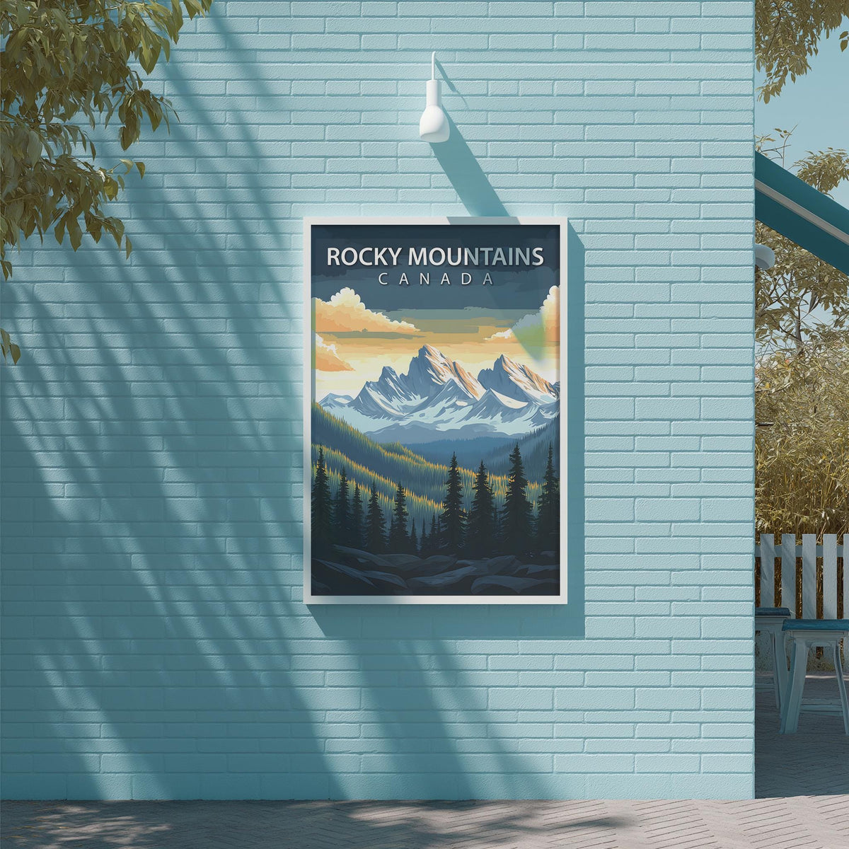 A framed poster of Rocky Mountains in Canada is displayed on a light blue brick wall, with a tree and a white light fixture above it.