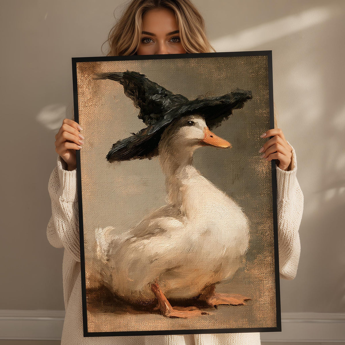 A woman holds up a framed painting of a duck wearing a witch's hat.