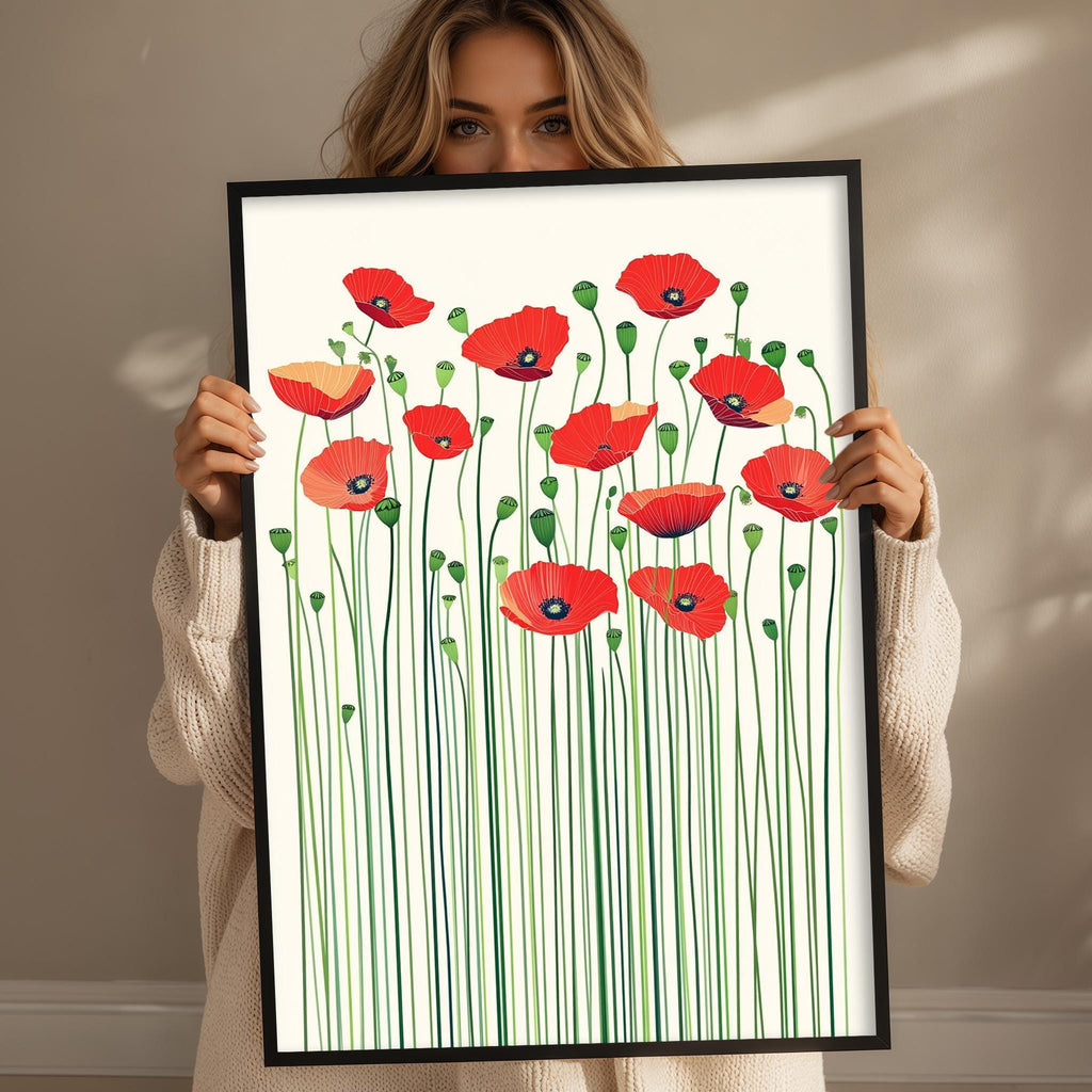 A woman is holding up a framed print of red flowers with green stems.