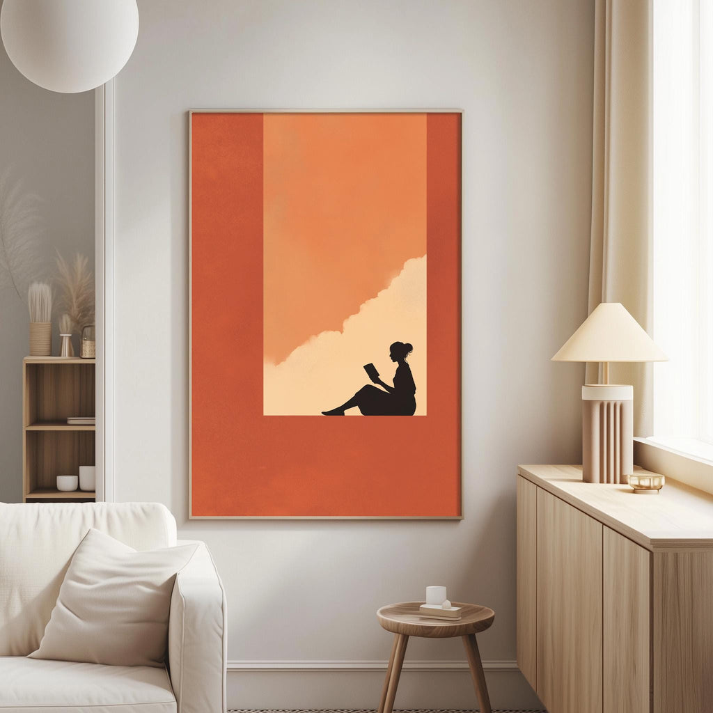 a living room with a large orange and black framed artwork depicting a woman sitting on a bench, reading a book. The artwork is hanging on the wall, and there is a white couch and a small table in the room.