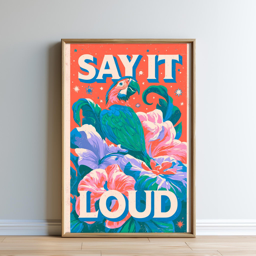 The image is a framed poster with a vibrant, colorful design featuring a parrot perched on a flower. The text "SAY IT LOUD" is prominently displayed in the center of the poster.