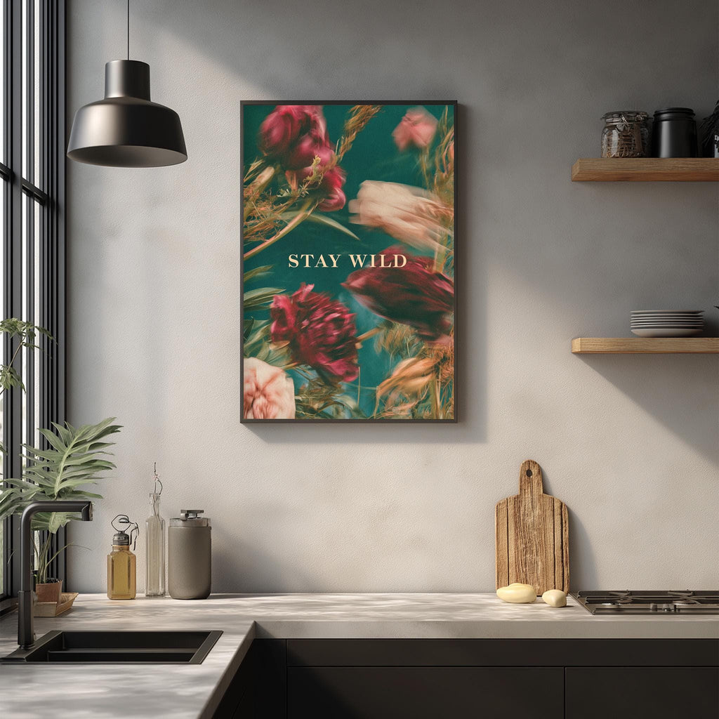 a kitchen counter with a framed poster of flowers hanging above it, along with various kitchen items such as a cutting board, a bottle, and a bowl.