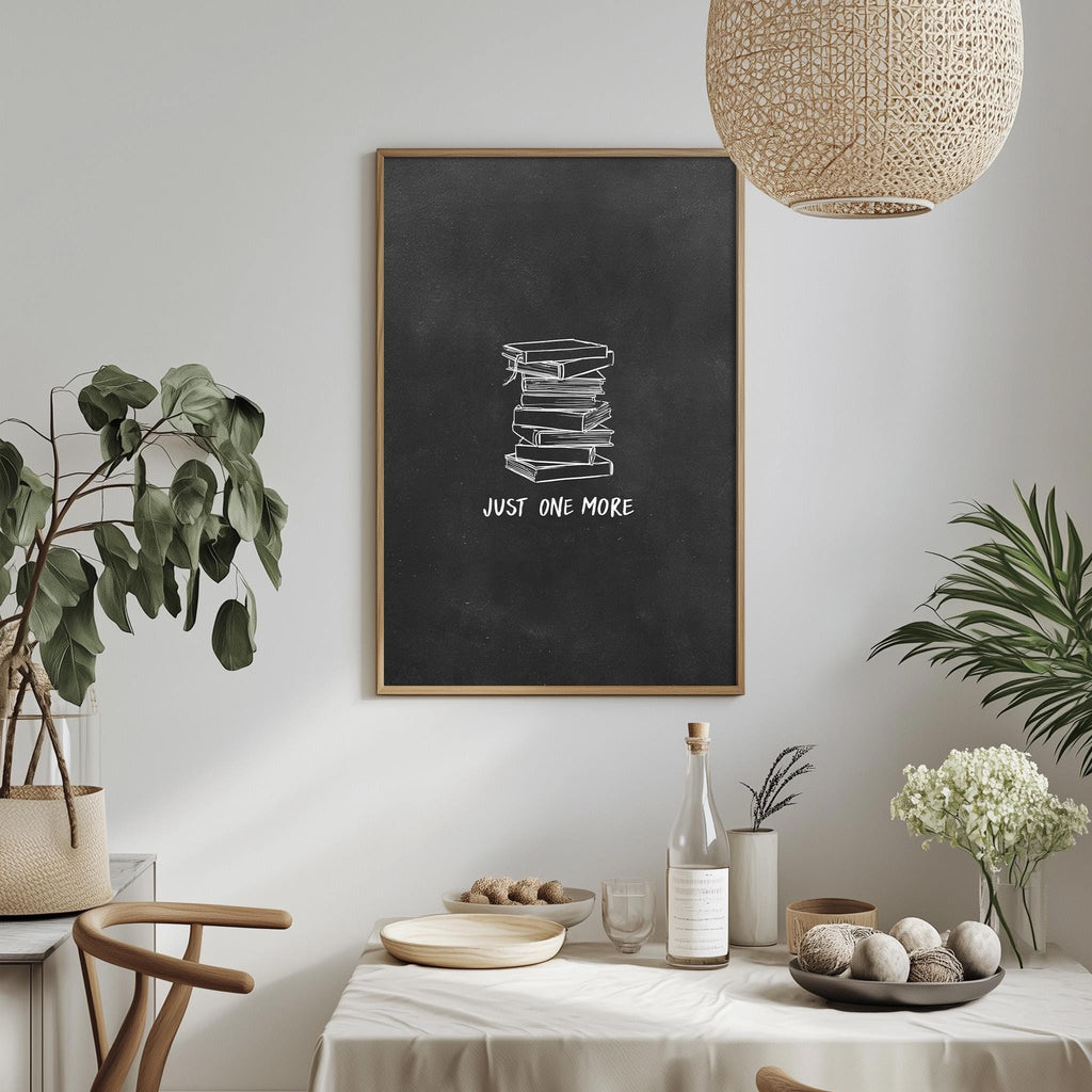 a dining table with a white tablecloth, a bowl of fruit, a bottle, and a vase with flowers. Above the table, there is a framed poster with the text "JUST ONE MORE" and a stack of books. The table is set with a variety of items, including a potted plant, a vase, and a bottle.