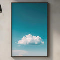 a kitchen counter with various kitchen items, including a cutting board, a soap dispenser, and a plant. Above the counter, there is a framed picture of a blue sky with a fluffy white cloud.