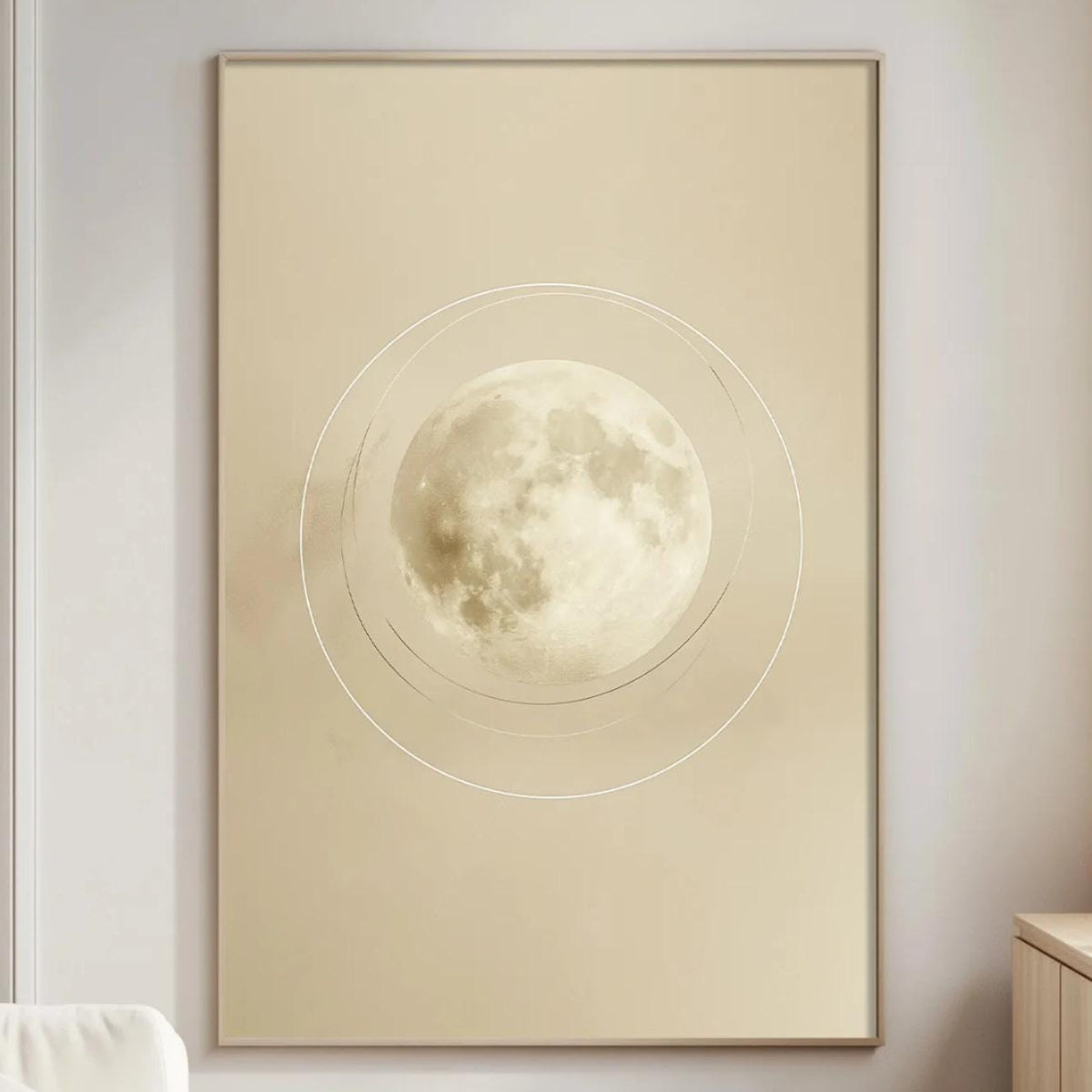 a serene living room with a large framed picture of a full moon hanging on the wall. The room is furnished with a white sofa, a wooden side table, and a lamp on a wooden cabinet. The overall color scheme of the room is neutral, creating a calm and peaceful atmosphere.