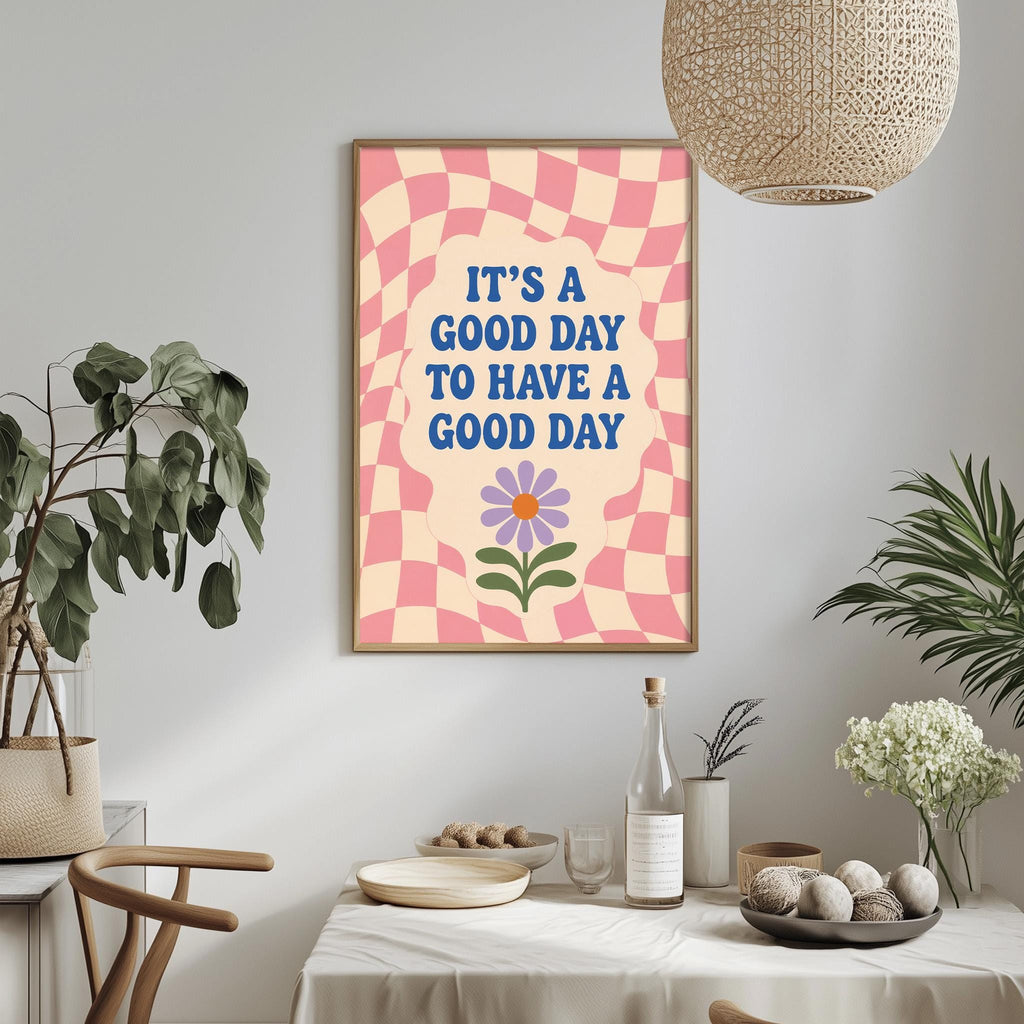 a framed poster with the text "It's a good day to have a good day" on it, hanging on a wall above a dining table with various items on it.