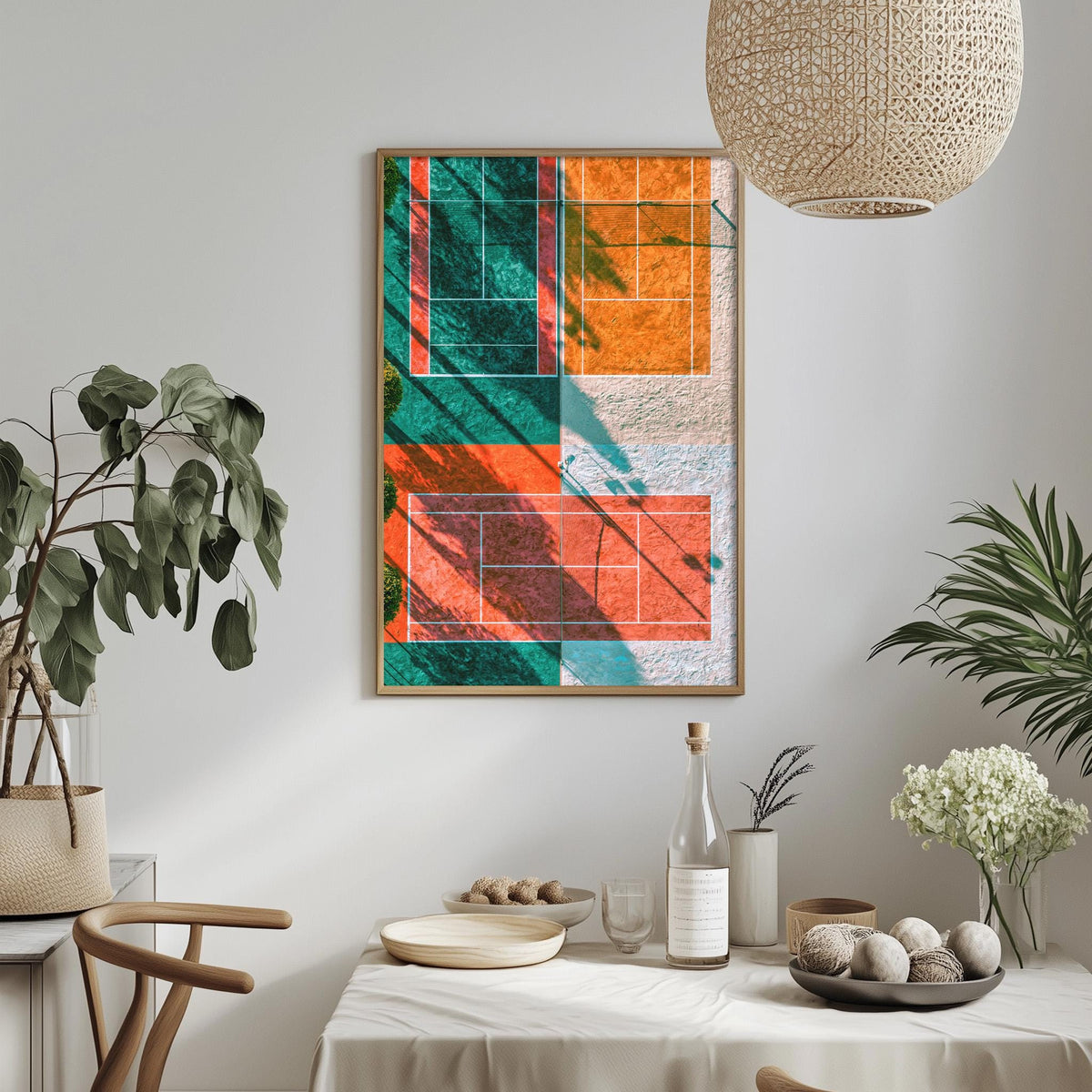 a dining table with a white tablecloth, a bowl of fruit, a bottle, and a vase with flowers. Above the table, there is a framed abstract painting with a geometric design in various colors.