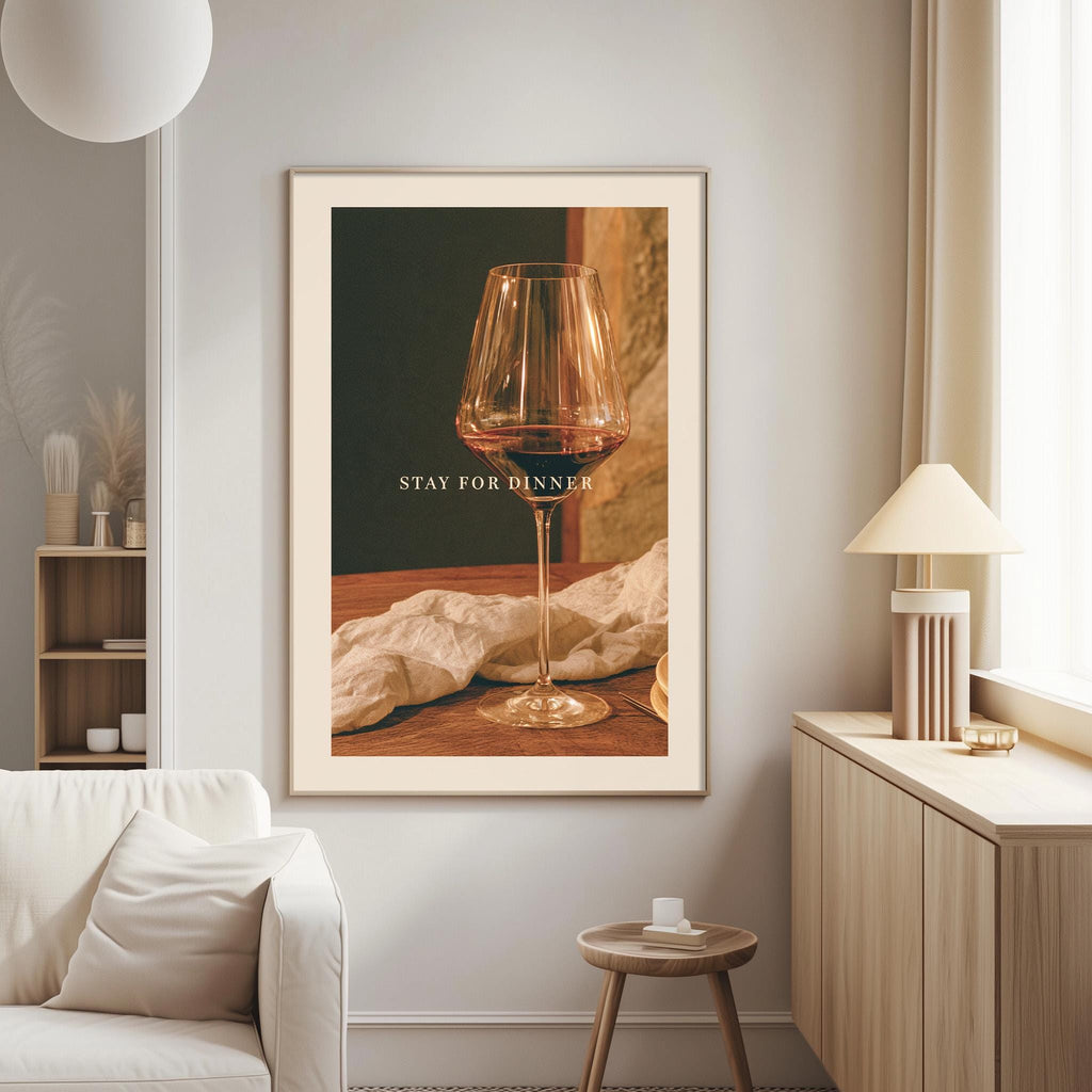 a framed photograph of a wine glass on a wooden surface, with the text "STAY FOR DINNER" displayed on the glass.
