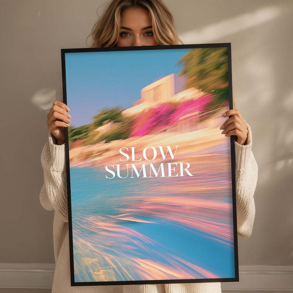 A woman holding a framed poster with a colorful beach scene and the text "SLOW SUMMER" on it.