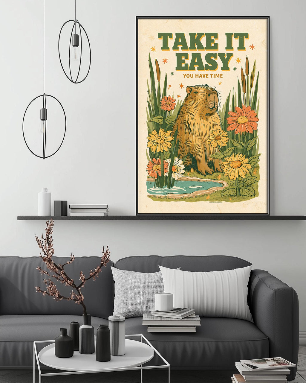 a framed poster with a beaver and flowers hanging on a wall above a gray couch with a coffee table in front of it.