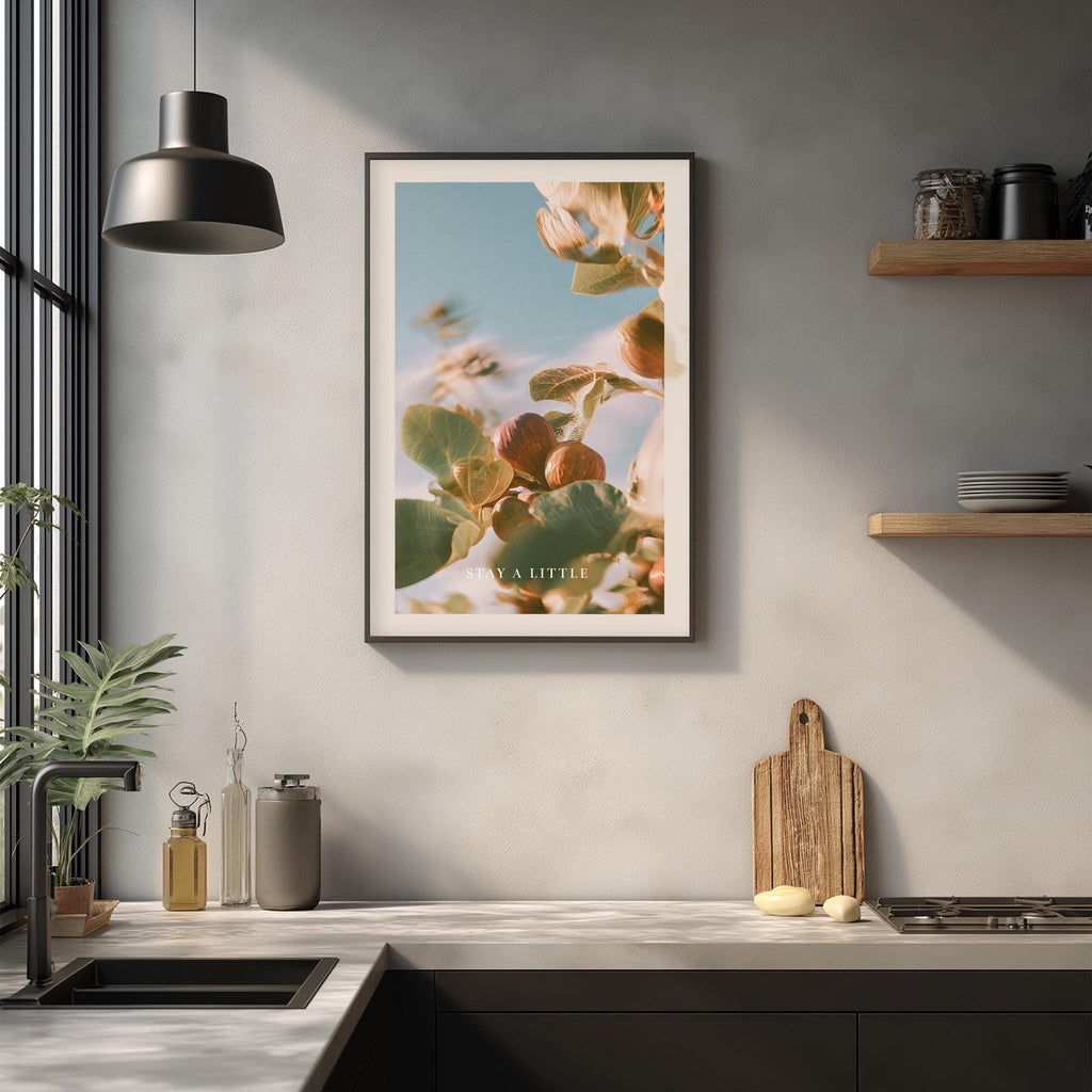 a kitchen counter with various items such as a cutting board, a soap dispenser, and a plant. Above the counter, there is a framed picture of a plant with flowers hanging on the wall.