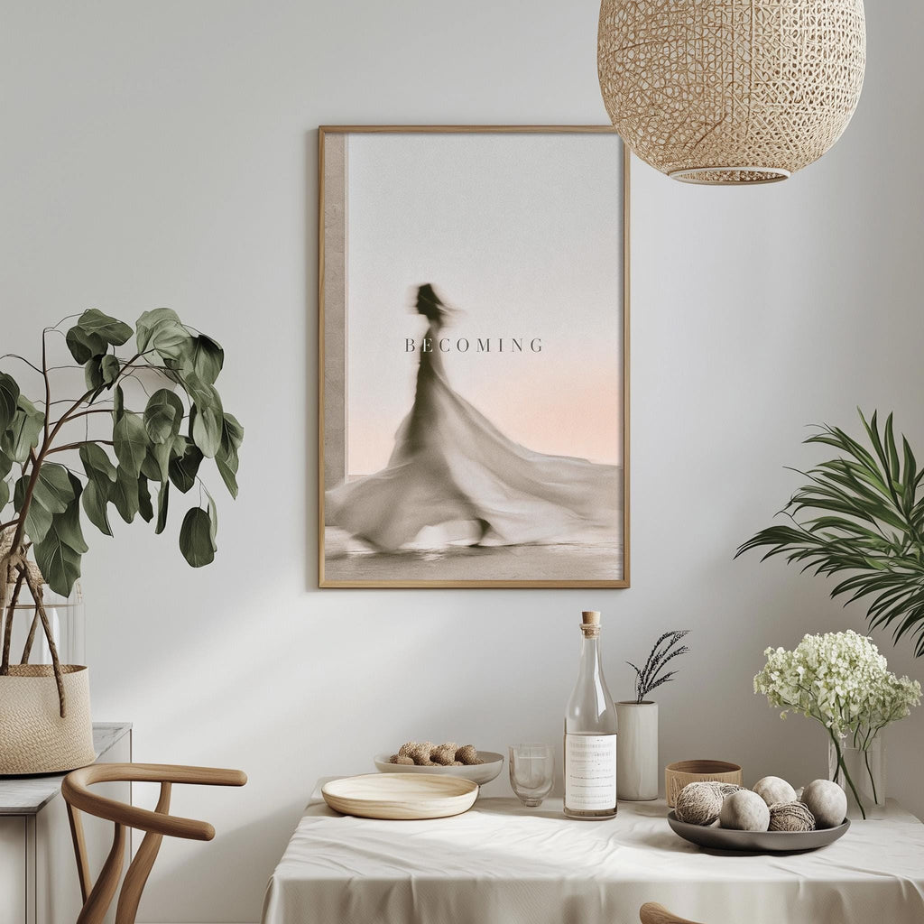 a dining table with a white tablecloth, a bowl of fruit, a bottle, and a vase with flowers. Above the table, there is a framed picture of a woman with a flowing dress. The table is set with a bottle, a wine glass, and a plate of food. The room has a minimalist and elegant design, with a pendant light hanging above the table and a plant adding a touch of greenery to the space.